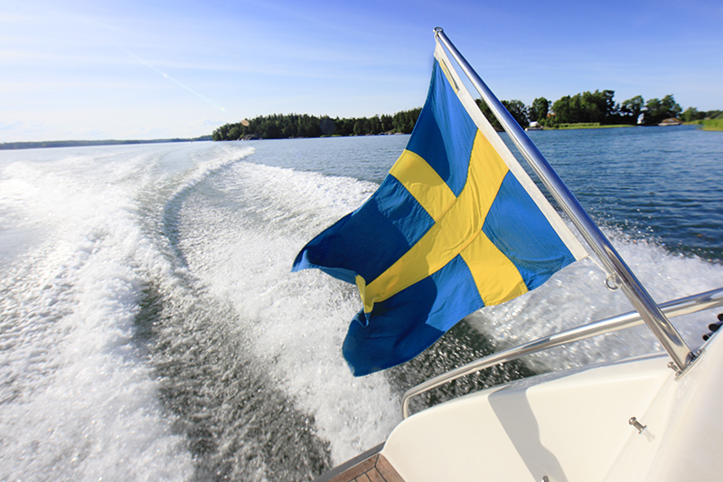 Bilden visar en svensk flagga och kölvattnet efter en båt.