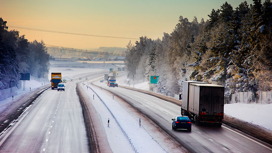 Några bilar och lastbilar åker på en motorväg i vinterlandskap