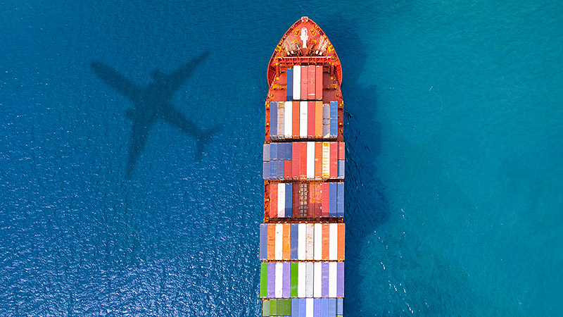 Fartyg med containerlast och skuggan från ett flygplan