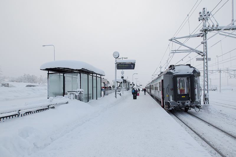 Tåg står på snöig perrong och resenärer är på väg att kliva på.