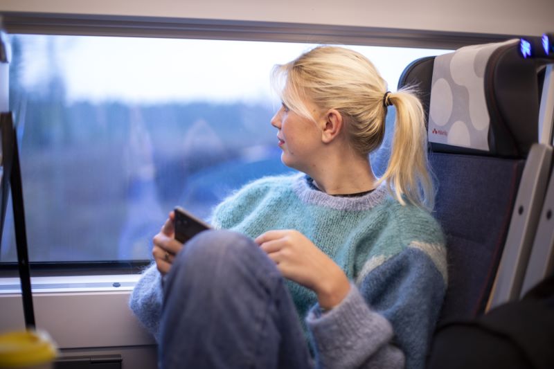 Kvinna sitter på tåg och tittar ut genom fönsterruta.