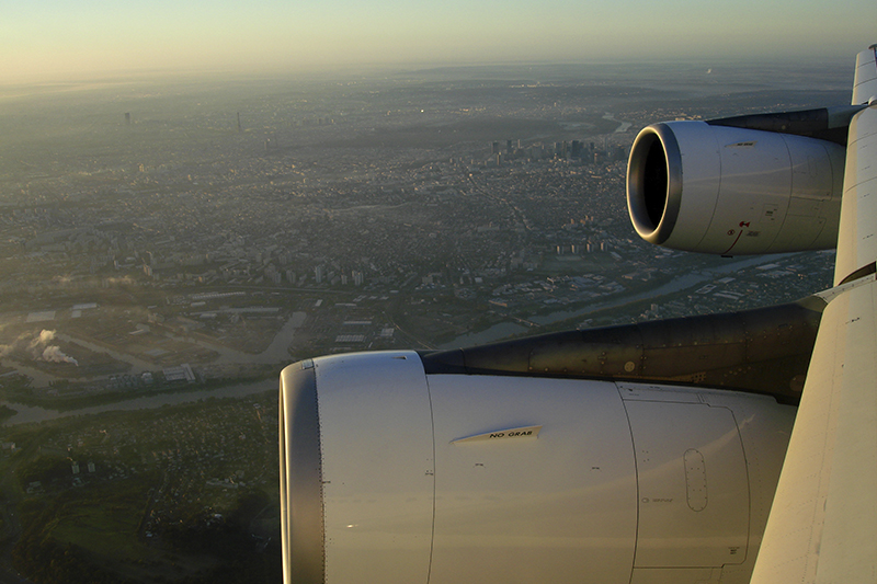 Bilden visar motorer på ett flygplan som flyger över en stad.